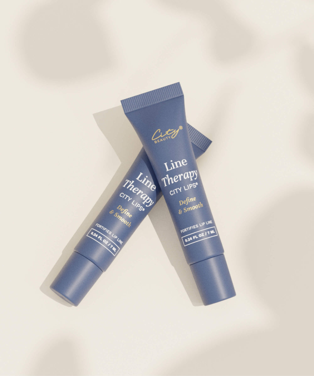 City Lips Line Therapy by City Beauty – lifestyle flatlay showing two closed navy blue tubes crossed on a warm beige background with soft natural shadows